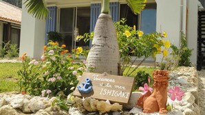Un letrero con 'Vacances à la mer ISHIGAKI' y una pequeña estatua de león frente a un edificio de fachada blanca y contraventanas azules.