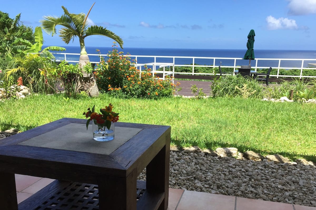 A patio with a table, a vase with flowers, a view of the ocean, and a white fence.