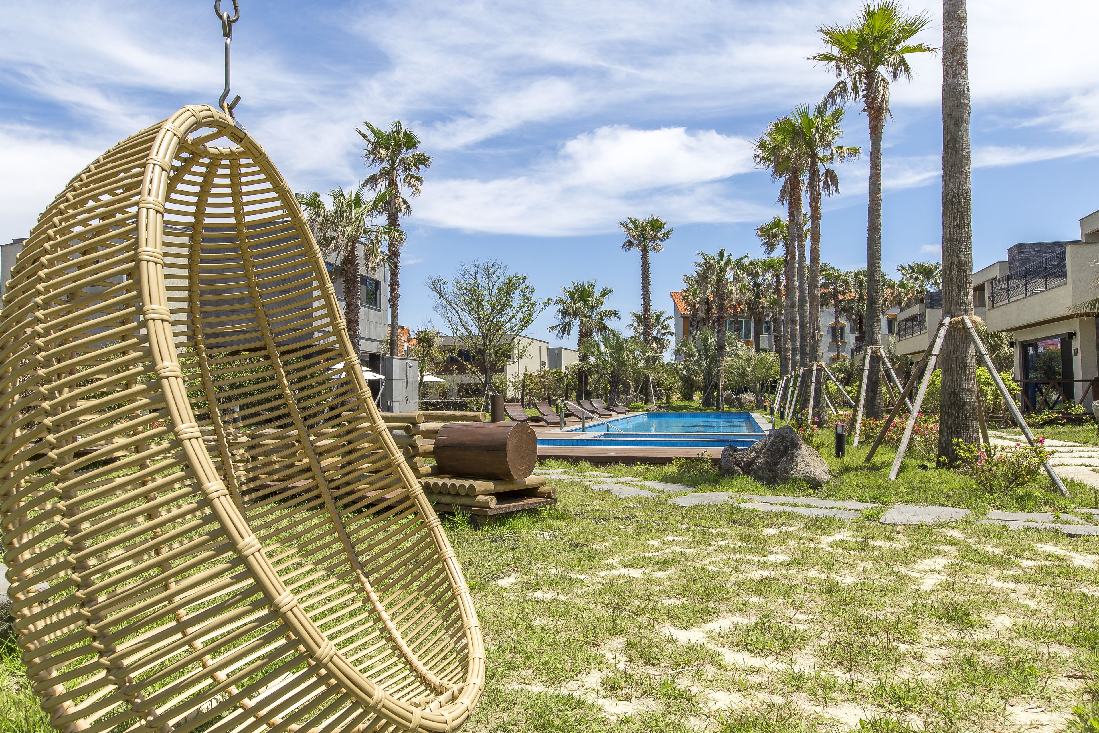 Une chaise en osier, une piscine, des palmiers et un bâtiment en arrière-plan.