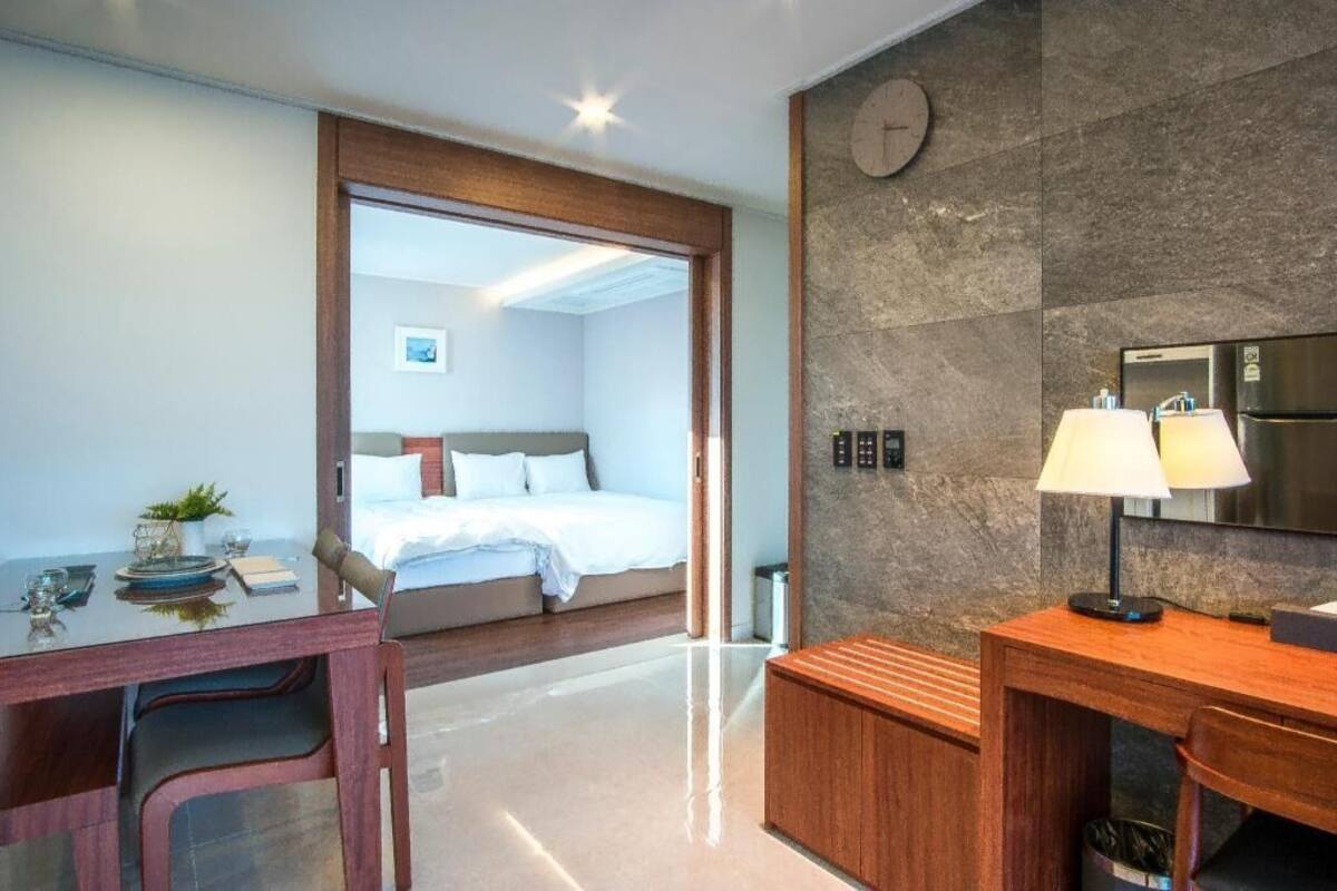 Une chambre d’hôtel avec un lit, un bureau doté d’une lampe, une horloge au mur et une vue sur une autre chambre.