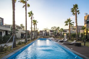 Ein Pool mit Liegestühlen und Palmen, umgeben von modernen Gebäuden.
