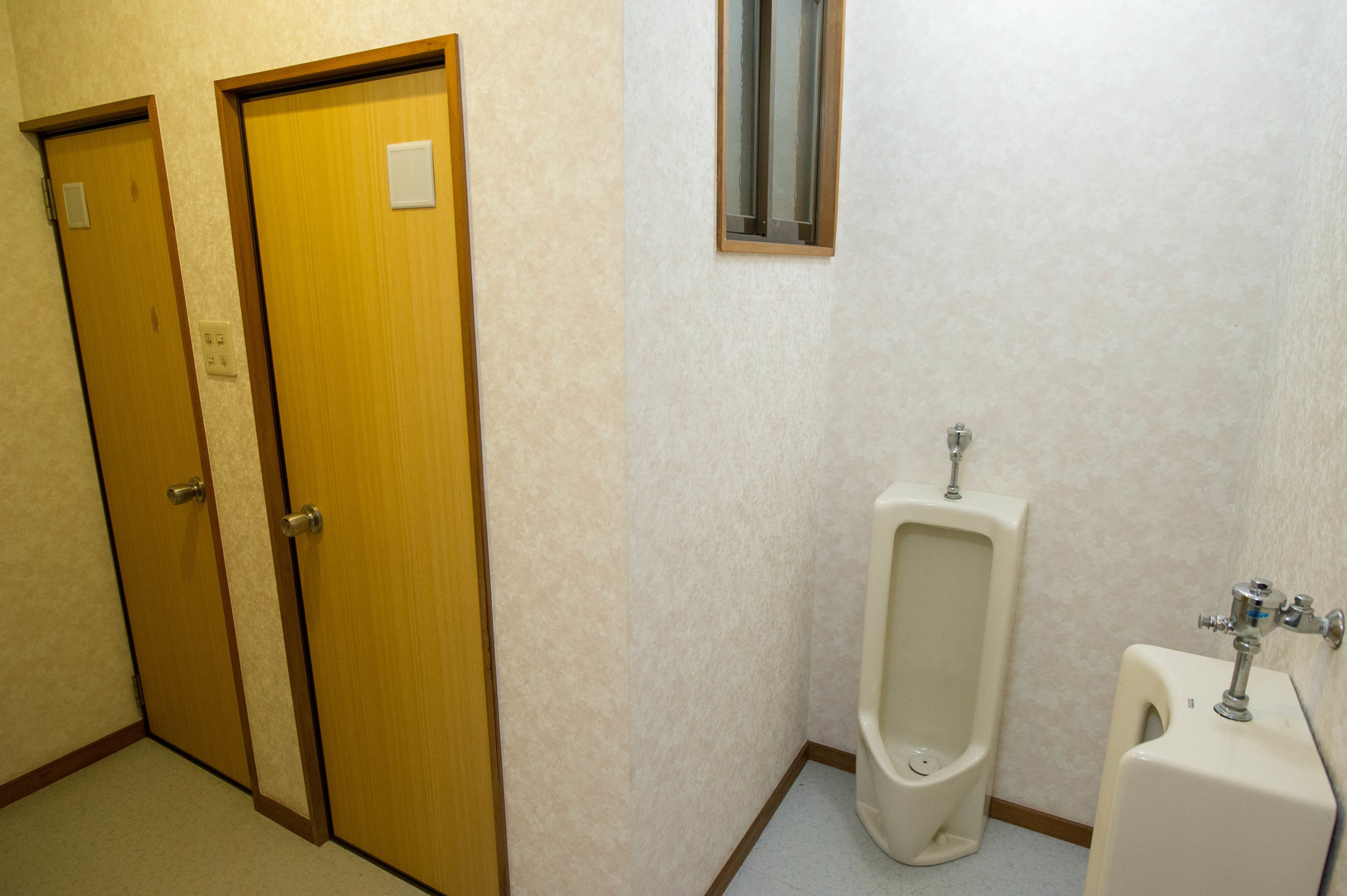 A men's restroom with two wooden doors, a urinal, and a toilet.