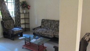 A living room with a zebra-patterned sofa, a wooden chair, and a glass coffee table. - Fortune Green Hotel (Murang'a)