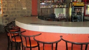 A bar area with a curved counter, four bar stools, and shelves stocked with bottles. - Fortune Green Hotel (Murang'a)