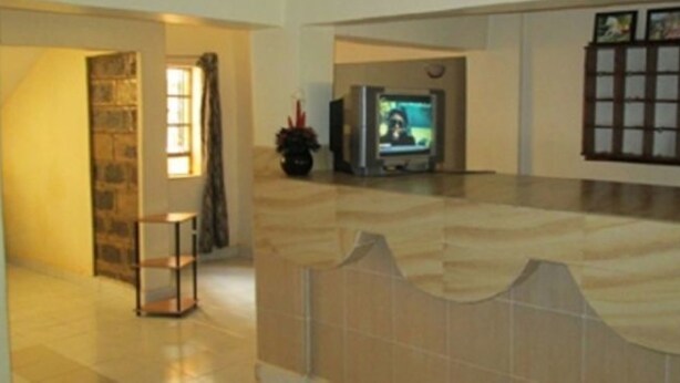 A living room with a tiled floor, a television, and a bookshelf. - Fortune Green Hotel (Murang'a)