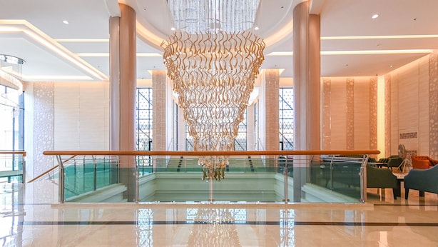 Een ruime lobby met een centraal hanglamp, glazen balustrades en een trap naar de bovenverdiepingen.