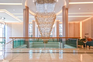 Een ruime lobby met een centraal hanglamp, glazen balustrades en een trap naar de bovenverdiepingen.