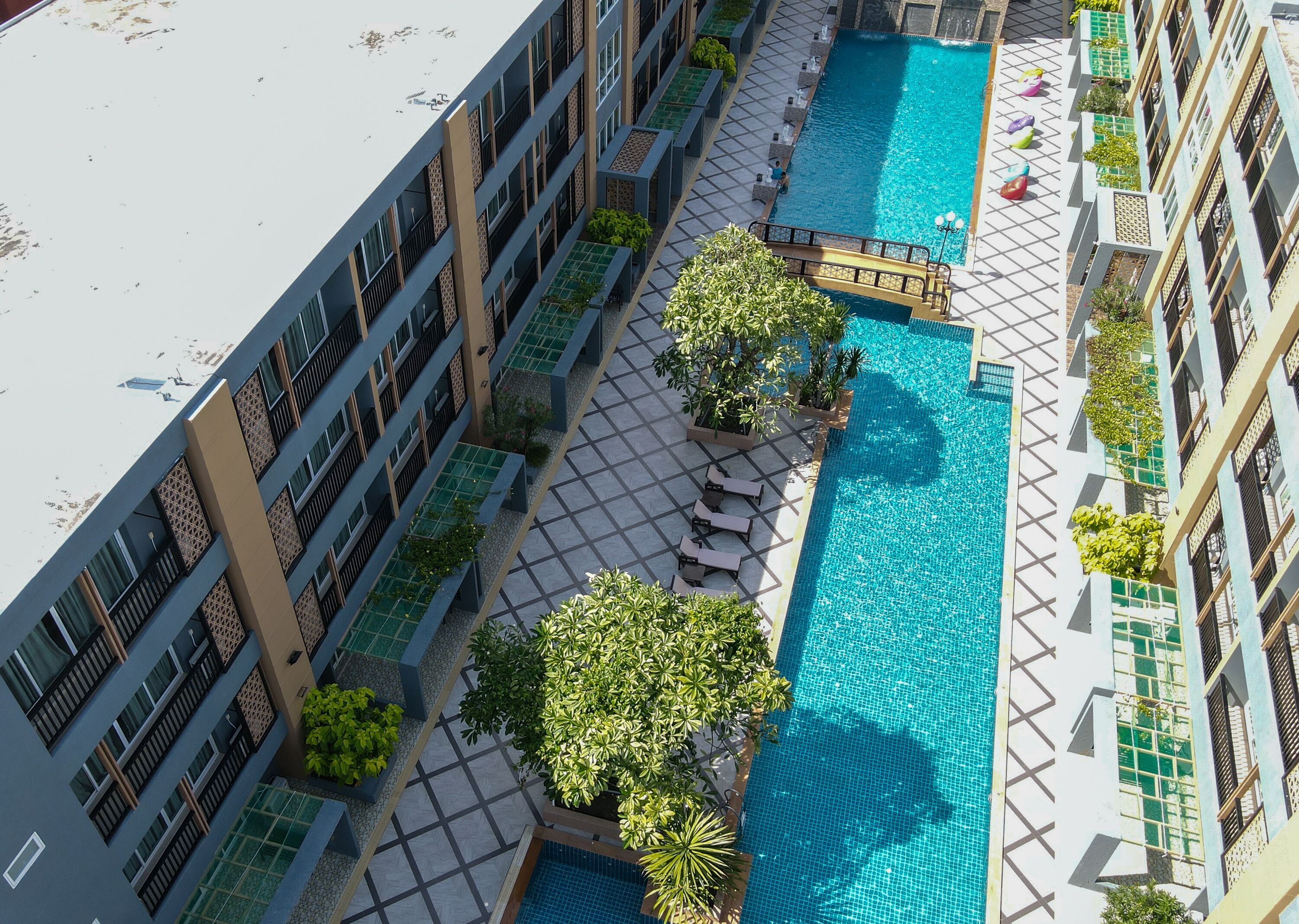 A rooftop swimming pool with a tiled deck, lounge chairs, and potted plants.