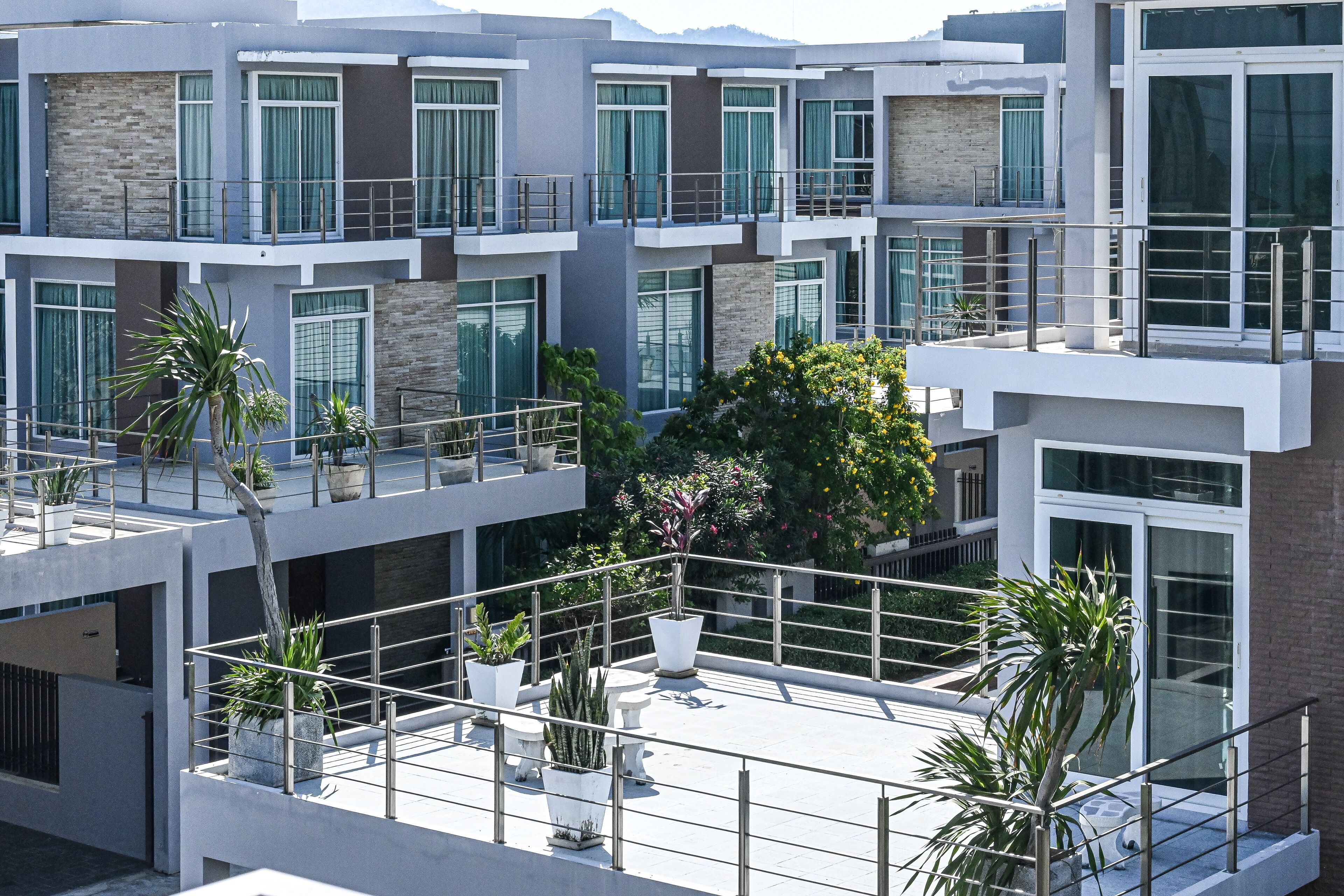 Un moderno edificio de varios pisos con balcones, plantas en macetas y ventanas amplias.