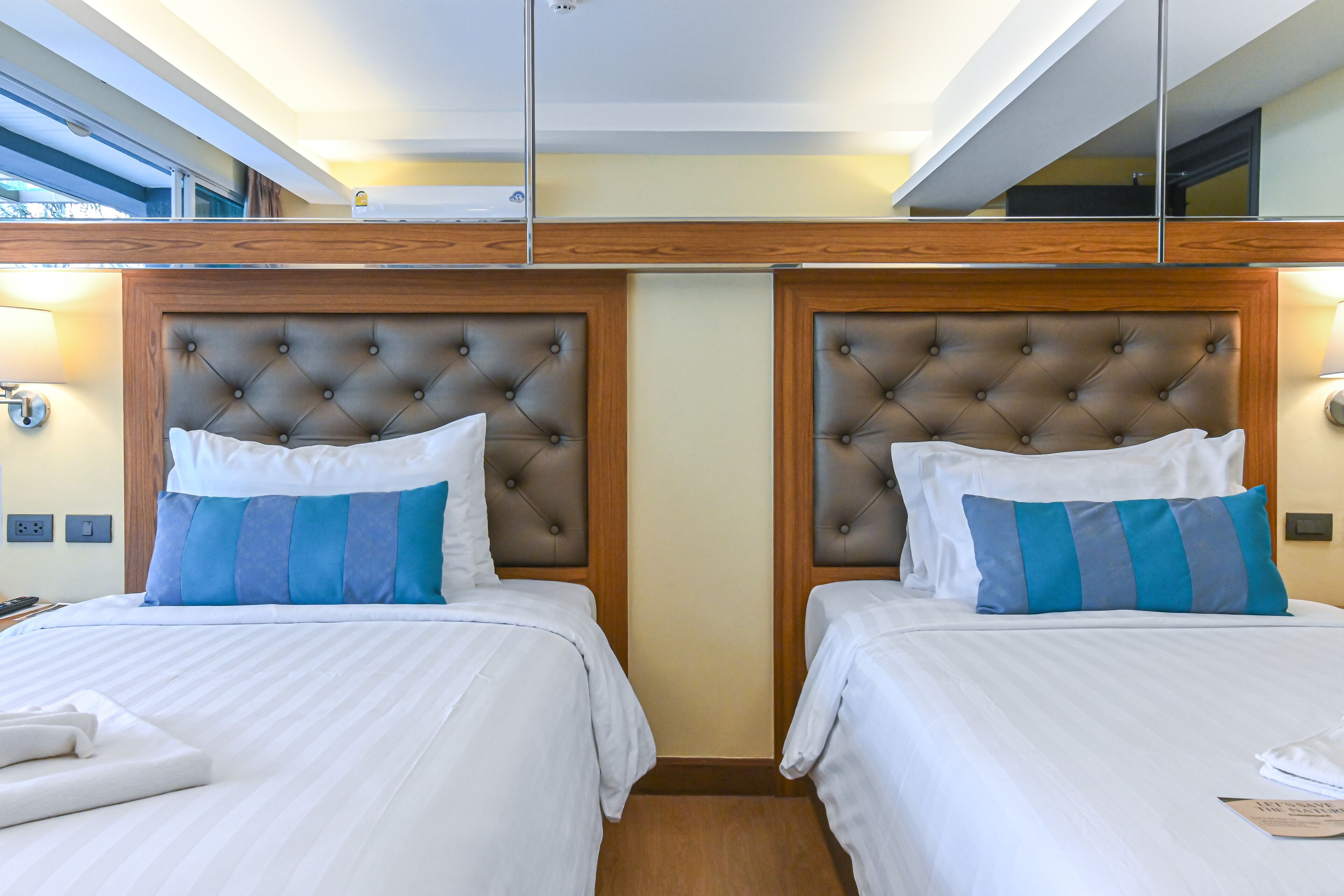 A hotel room with two beds, each with a tufted headboard and striped pillows.