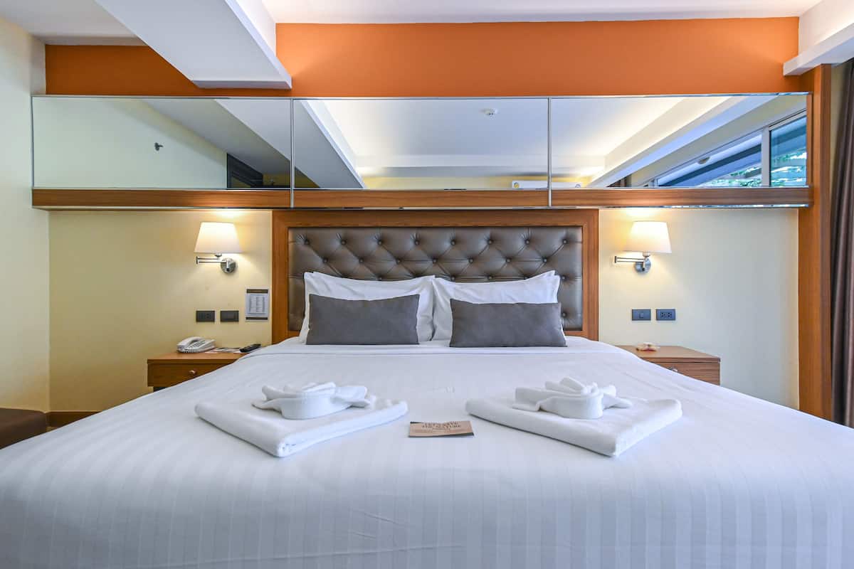 A hotel room with a large bed, two bedside lamps, a telephone, and a mirror above the bed.