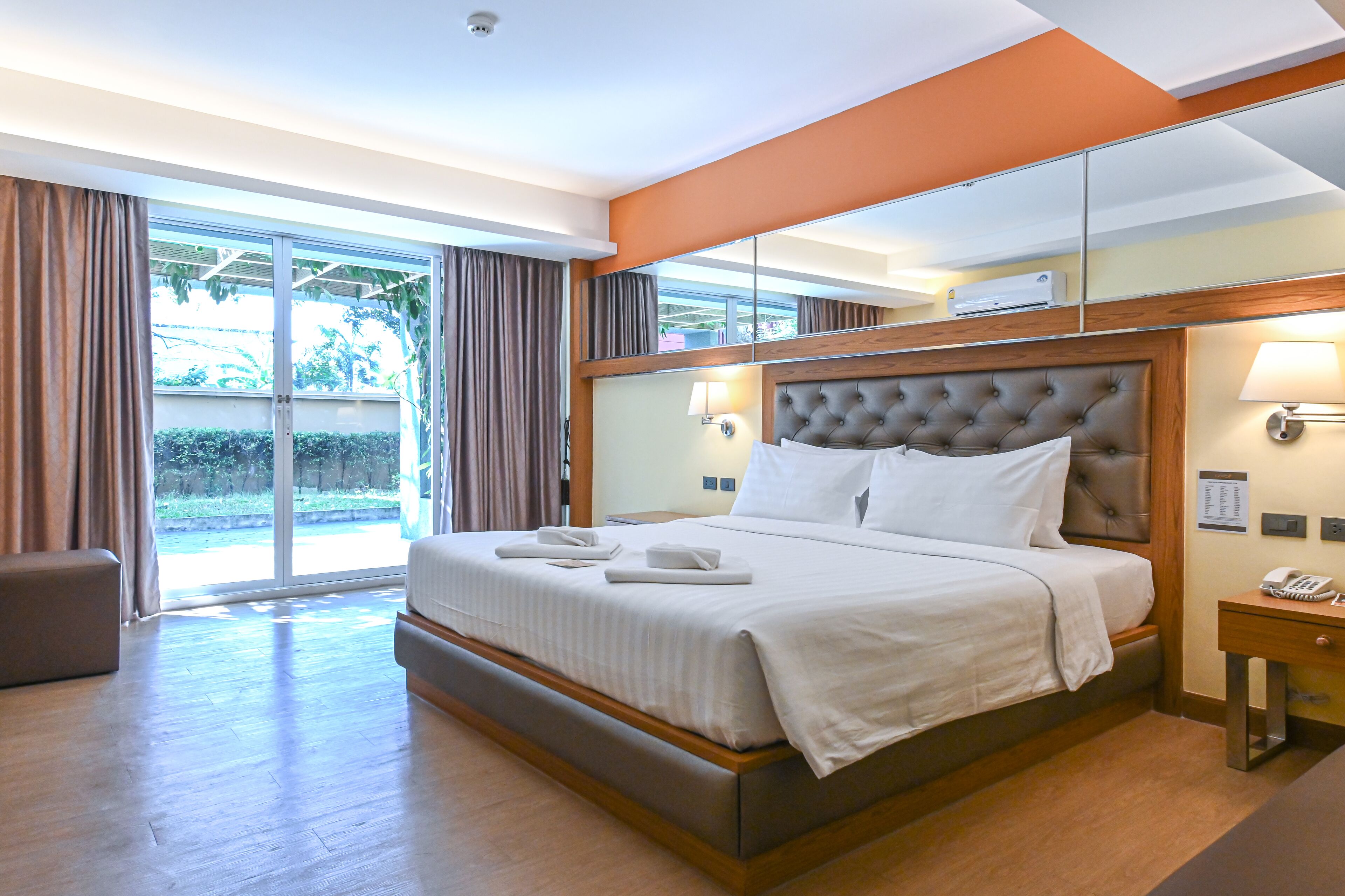 Ein Hotelzimmer mit einem großen Bett, einem Holz-Kopfende, einem Nachttisch mit Lampe und einem großen Spiegel.