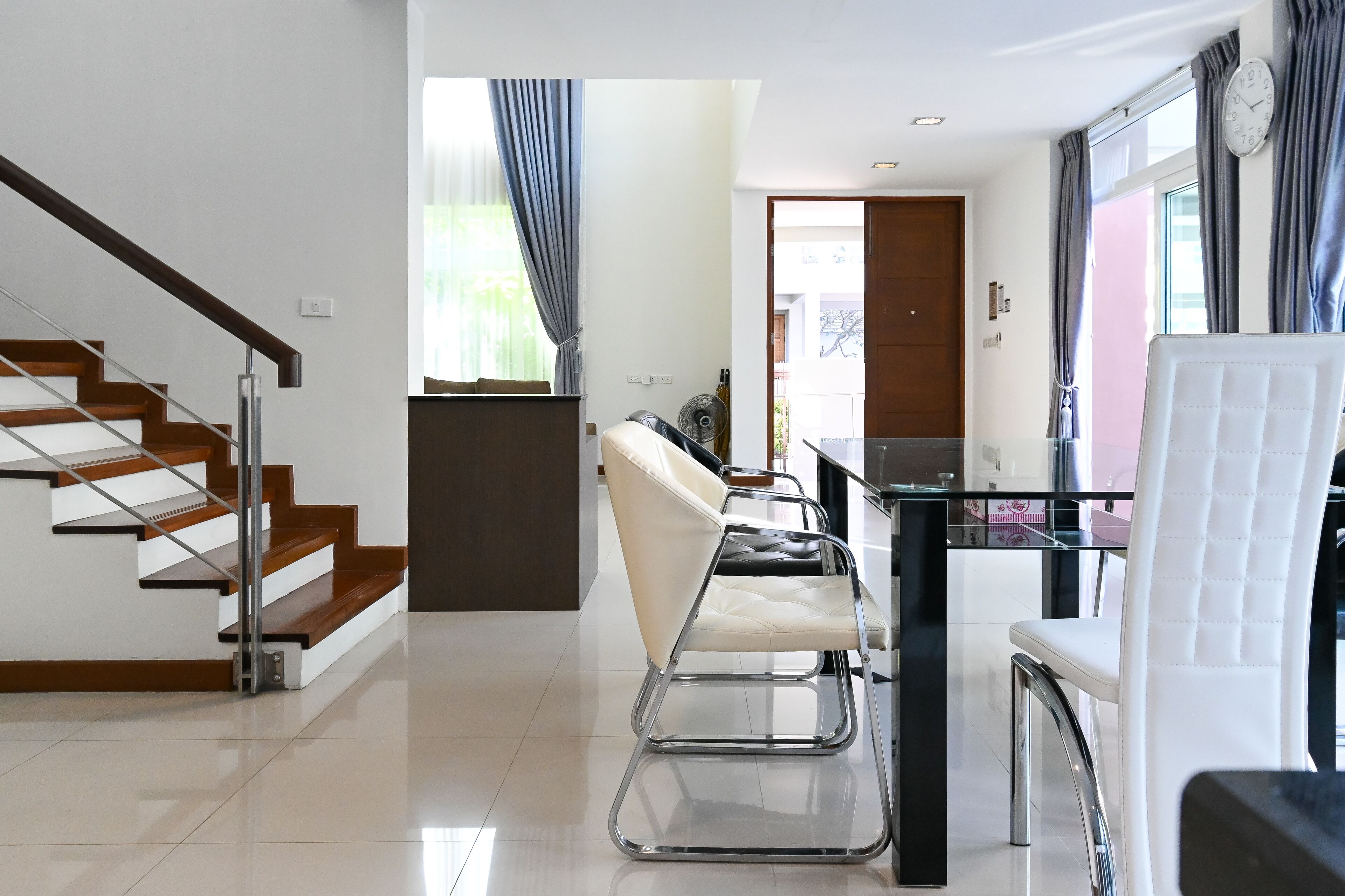 Un interior moderno con una escalera, un comedor con sillas y vistas a través de una ventana.