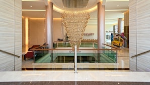 Een modern interieur met een centrale decoratieve constructie, glazen balustrades en een zichtbaar restaurant genaamd 'Grand Ballroom'.