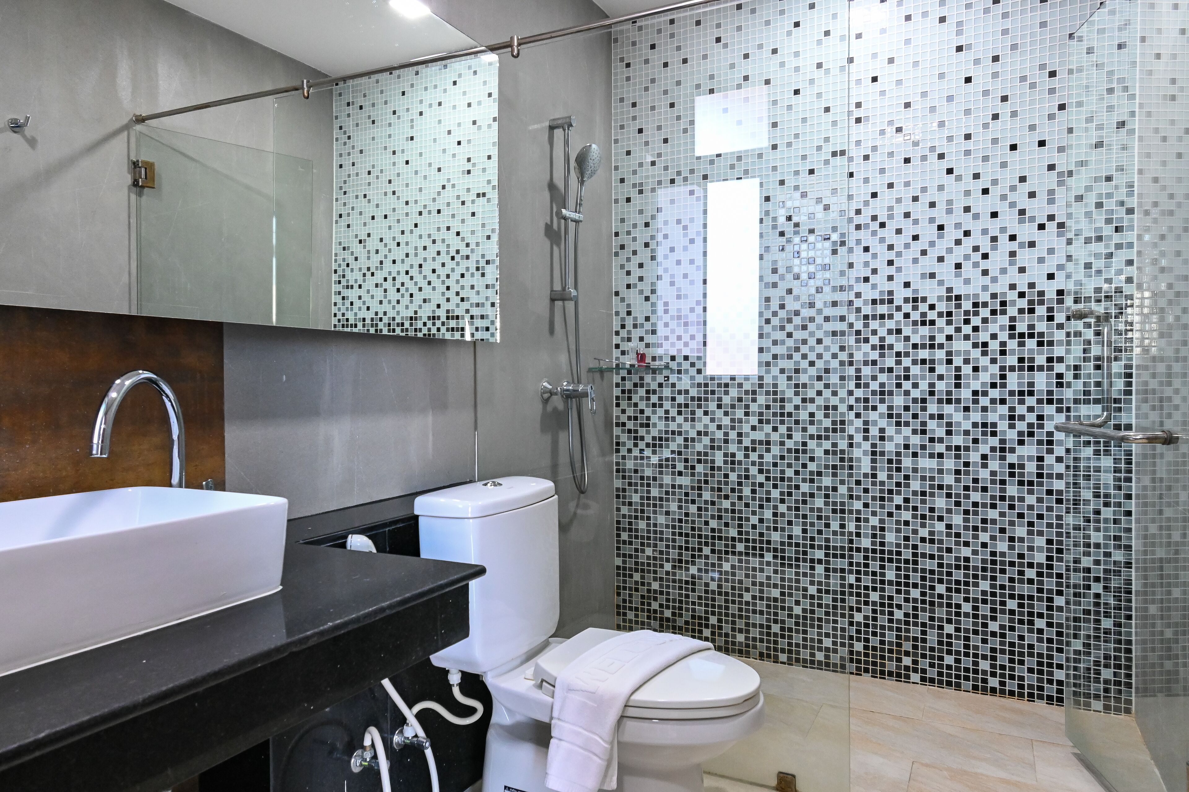 Un baño moderno con un espejo grande, un lavabo blanco, un inodoro y una zona de ducha.