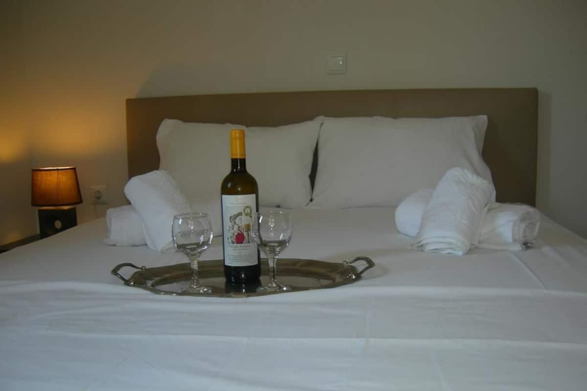 A neatly made bed with a tray holding a bottle and two glasses, a lamp, and a pillow on the headboard.