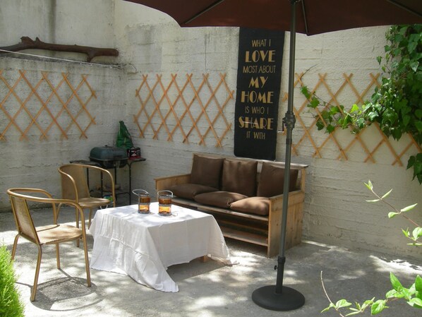 An outdoor seating area with a table, chairs, and a couch. There is a sign on the wall and a wooden lattice structure. - Sweet Home Palio (Kavala)