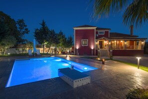 Una piscina con idromassaggio, circondata da un patio con illuminazione esterna.