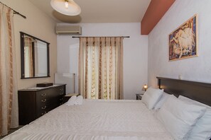 A hotel room with a large bed, a dresser, a mirror, a radiator, and a painting on the wall. - Villa Froso (Zakynthos)