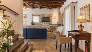 A living room with a stone fireplace, a blue sofa, and a wooden coffee table. - Villa Froso (Zakynthos)