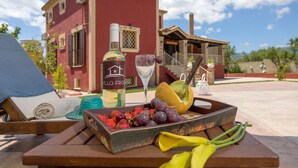 A wooden table with a bottle of wine, a glass, and a fruit basket containing grapes and melon. - Villa Froso (Zakynthos)