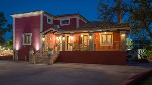 A two-story house with a red exterior, a stone staircase, and a balcony with railings. - Villa Froso (Zakynthos)