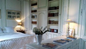 A bedroom with a bed, a nightstand, a bedside table with books, a dresser, and a bookshelf filled with books. - Château de Beaulieu (Saumur)