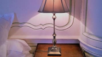 Een net opgemaakt bed met witte lakens en één wit kussen, een klein houten nachtkastje met een lamp, en een lijst met een afbeelding boven het bed.