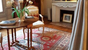 A traditional room with a wooden cabinet, a round table with a chair, a patterned rug, and a fireplace with a clock and decorative items. - Château de Beaulieu (Saumur)
