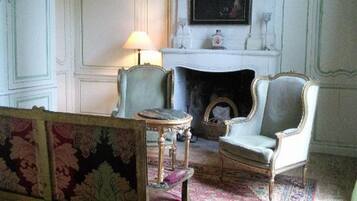 Une pièce avec une cheminée, deux fauteuils, une petite table et un tapis à motifs.