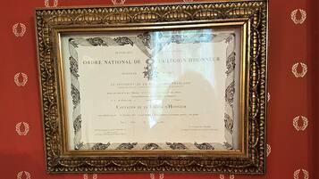 A framed certificate with ornate gold detailing and a red background with laurel patterns.