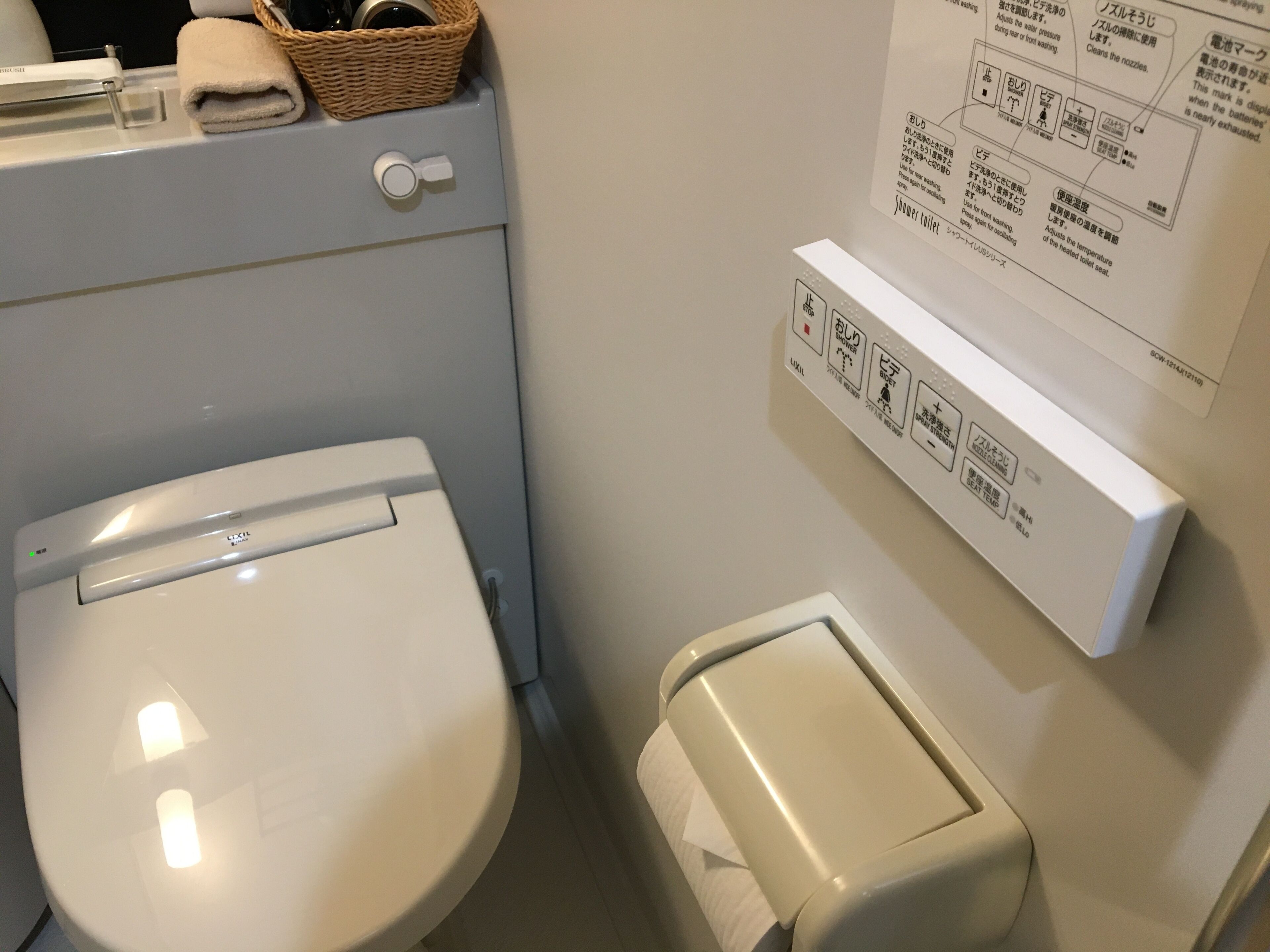 A bathroom with a toilet, a paper towel dispenser, and a wall-mounted instruction manual.