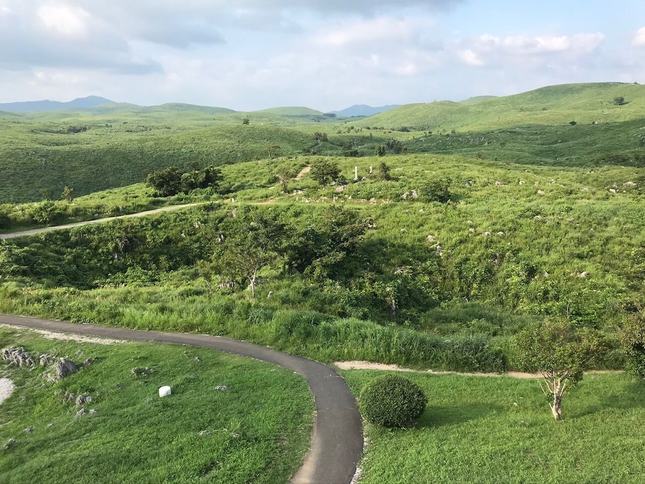 A winding road through a lush green landscape with rolling hills in the background.