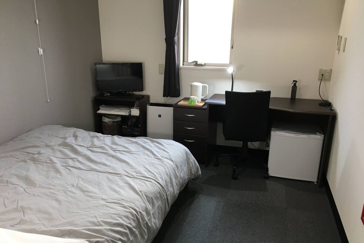 A hotel room with a bed, a desk with a computer, a small fridge, and a television.