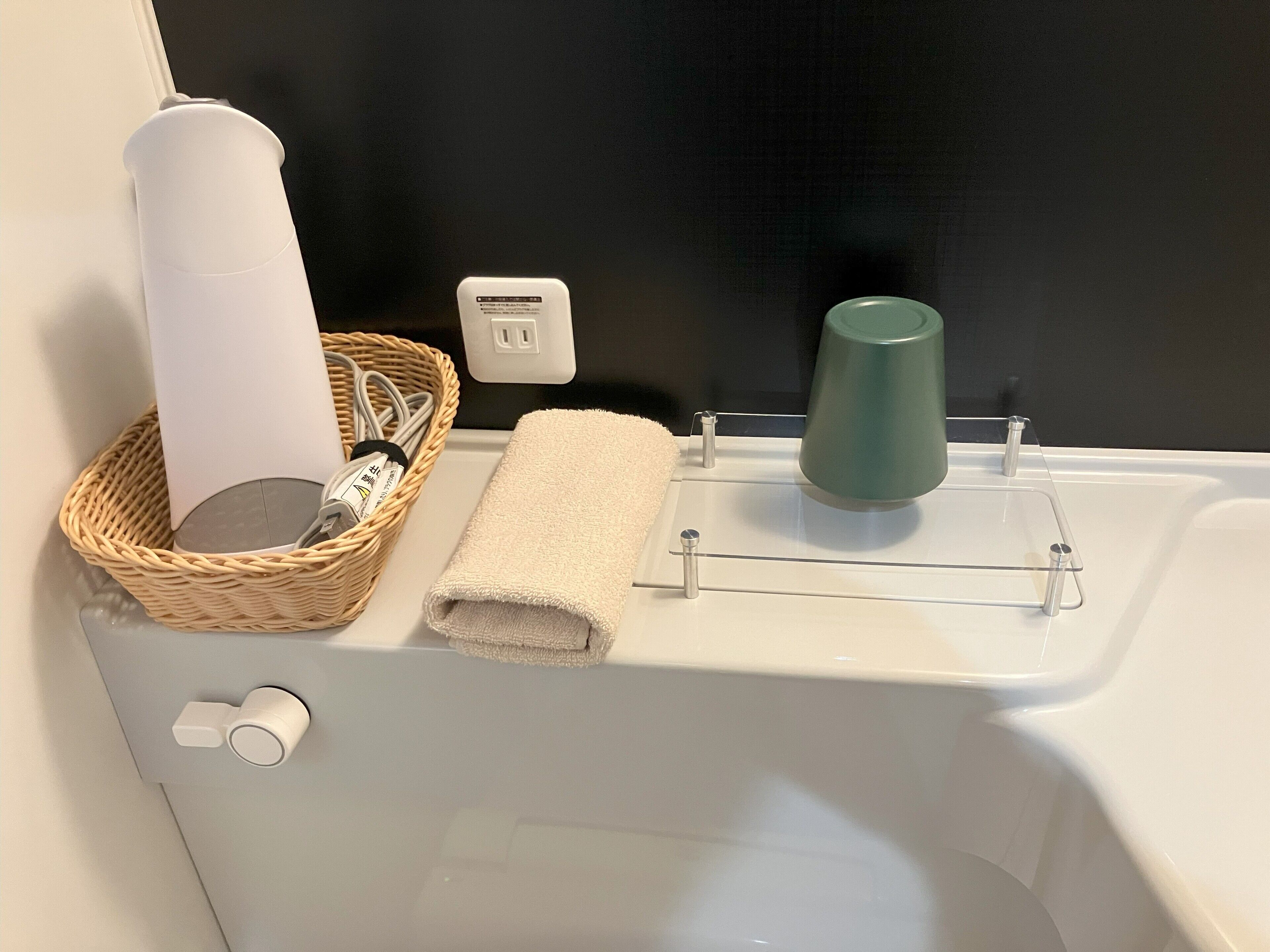 A bathroom with a white sink, a green cup, a white towel, and a wicker basket with a bottle and a toothbrush.