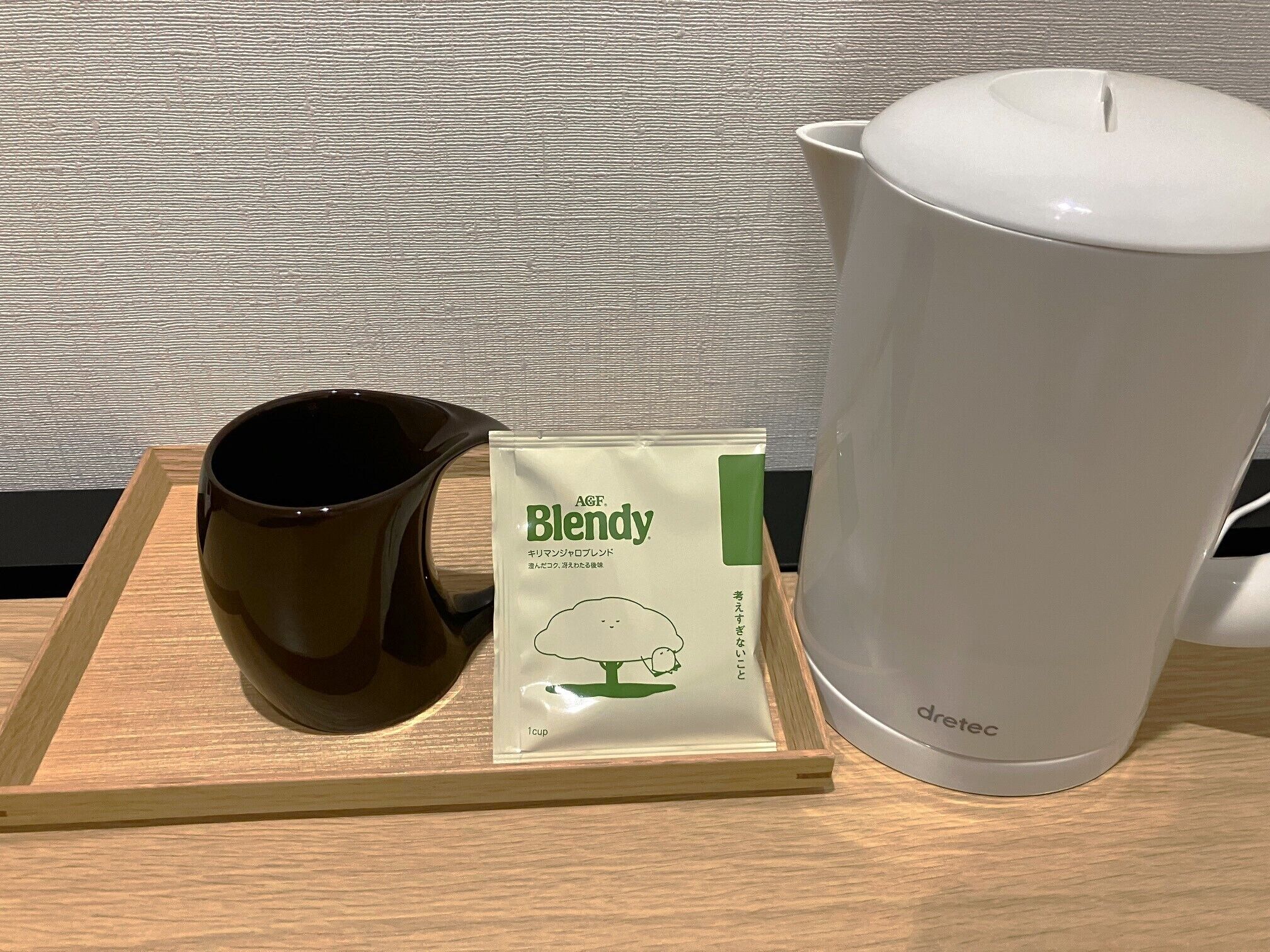 A wooden tray with a brown mug, a packet of tea labeled 'Blendy', and a white electric kettle on a table.