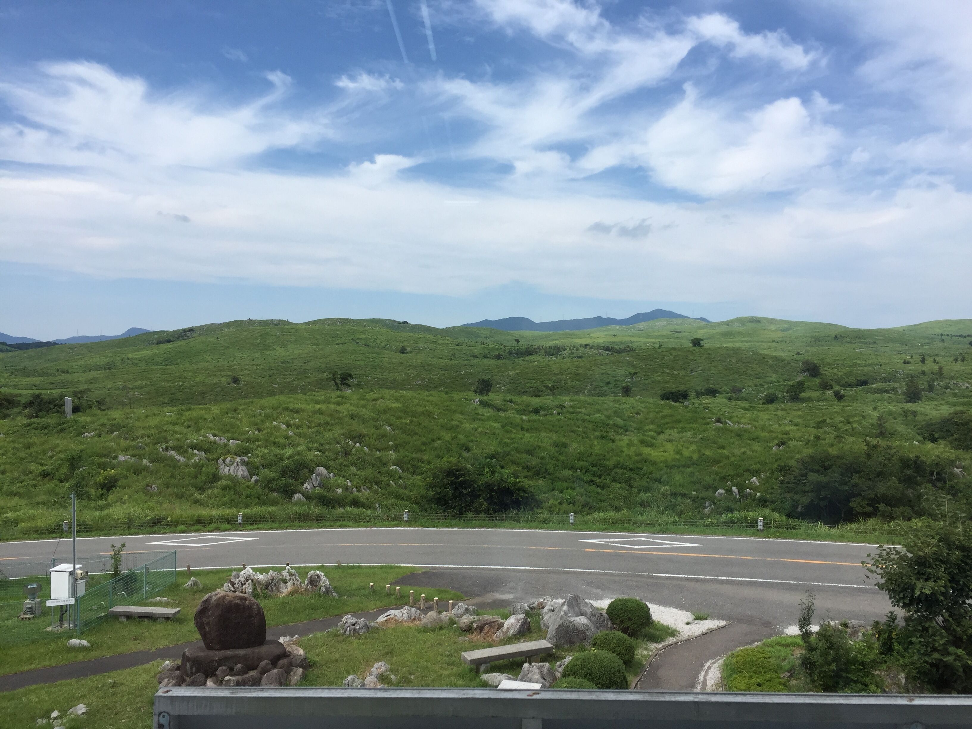 A view of a green landscape with a road and a fenced area with rocks and bushes.