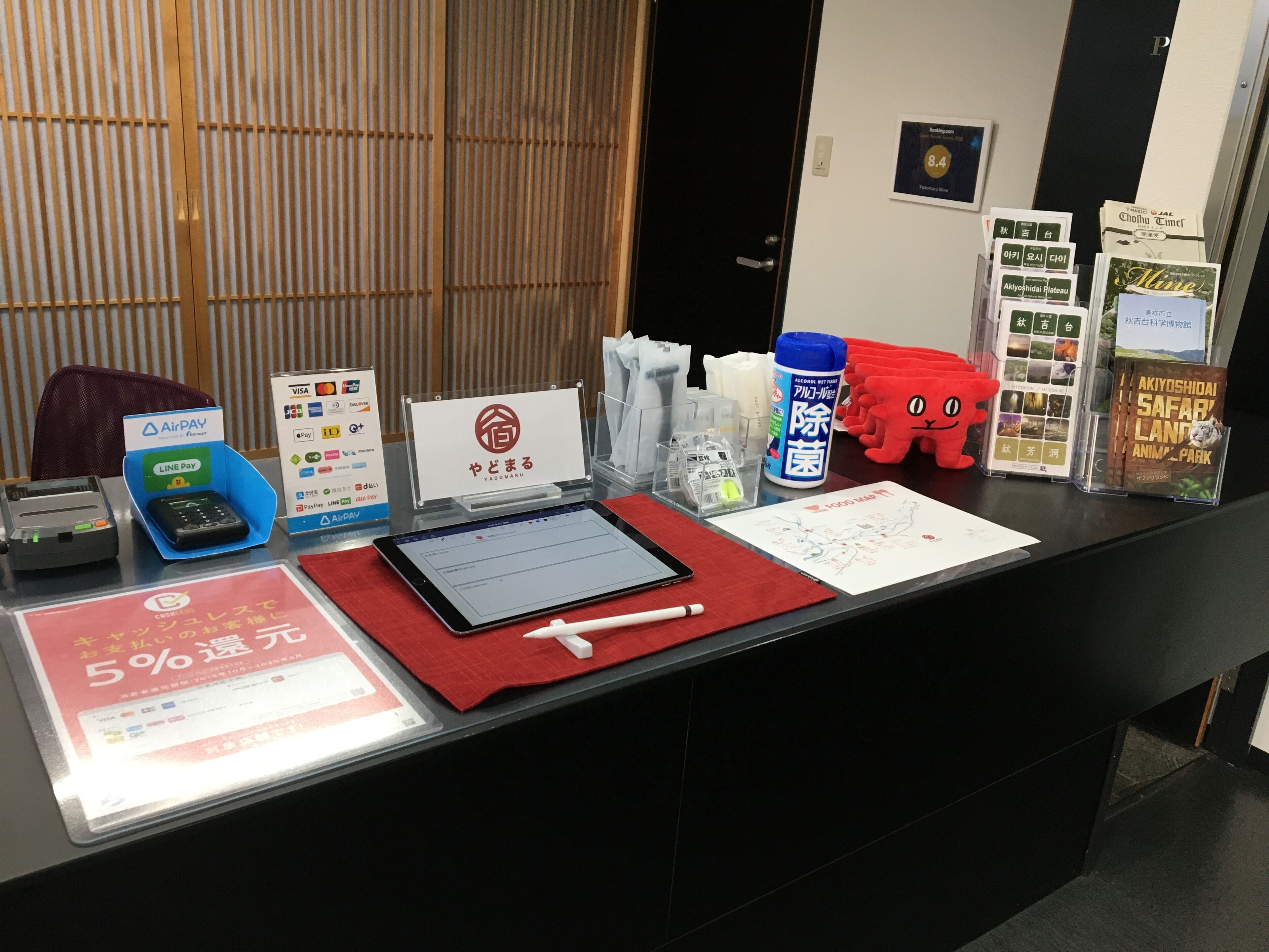 A reception desk with a tablet, a cash register, a Visa sign, a red mat, a water bottle, and informational brochures.