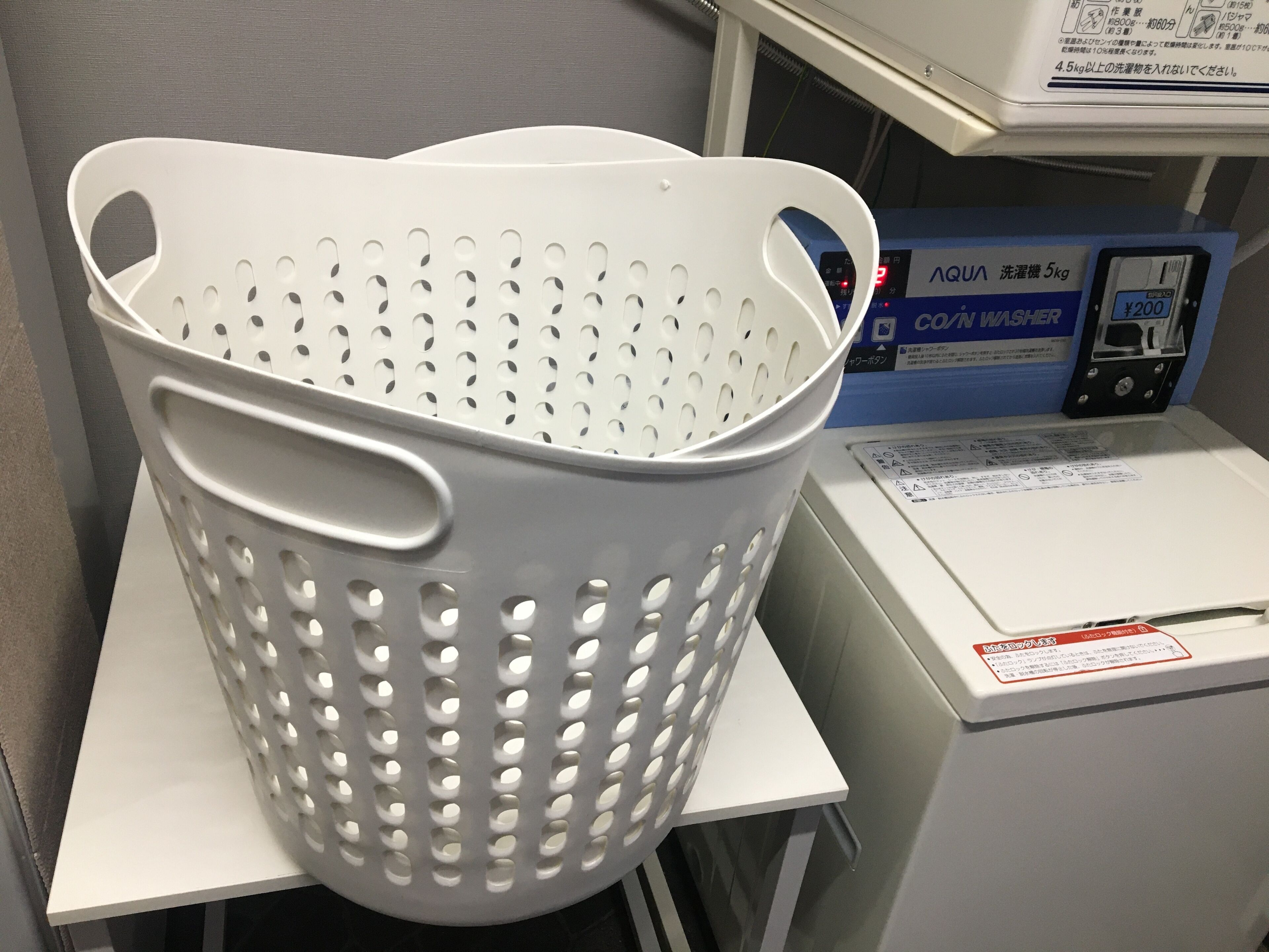 Un panier en plastique blanc, percé de trous, posé sur une surface blanche, à côté d’une machine à laver.