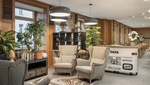 A spacious hotel lobby with two armchairs, a sofa, a bookshelf, and a TATA bus parked in the background. - myNext - Hotel Rudy (Vienna)