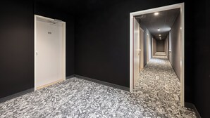 A hallway with patterned carpet, a door labeled "20", and a corridor leading to another room. - myNext - Hotel Rudy (Vienna)