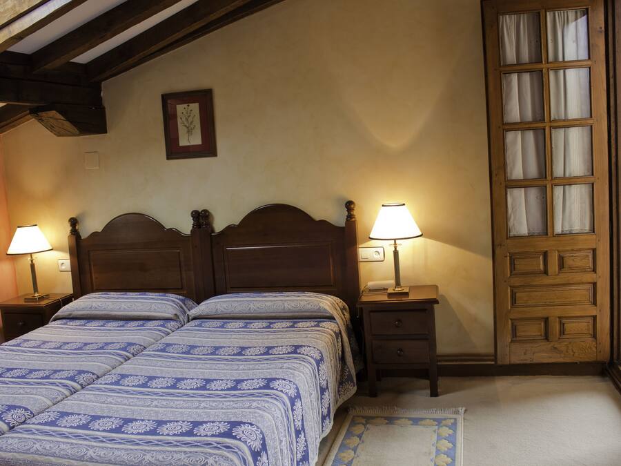 A bedroom with two beds, wooden headboards, bedside lamps, a framed picture on the wall, and a wooden door with glass panels.