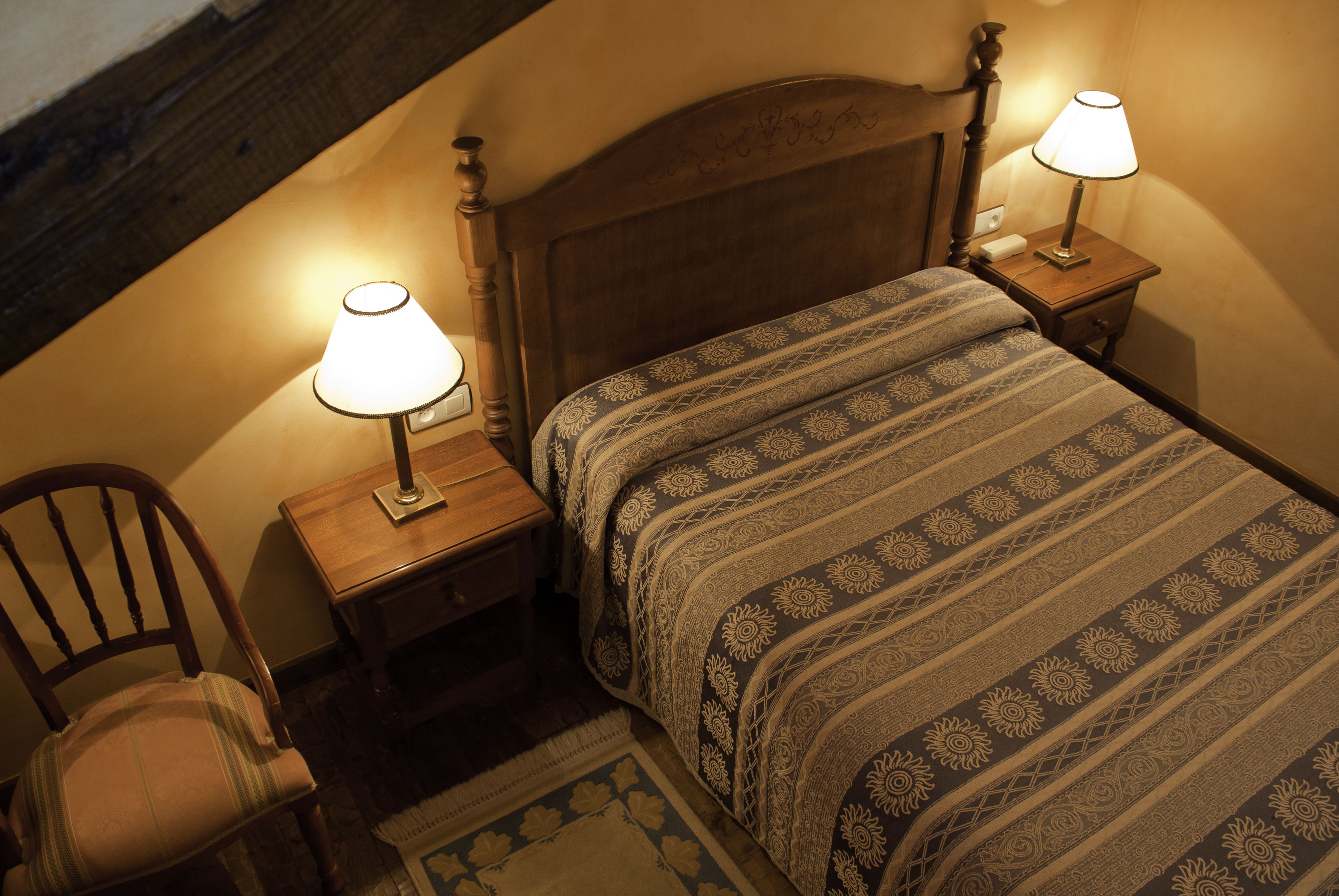 Una cama bien hecha con un edredón estampado y dos lámparas de noche.