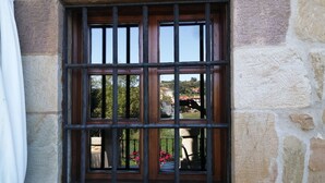 A window with a metal grille, stone wall, and a view of a garden with flowers. - Posada La Casa del Organista (Santillana del Mar)