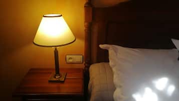 Un comodino con una lampada, una presa elettrica e un letto con cuscino bianco.