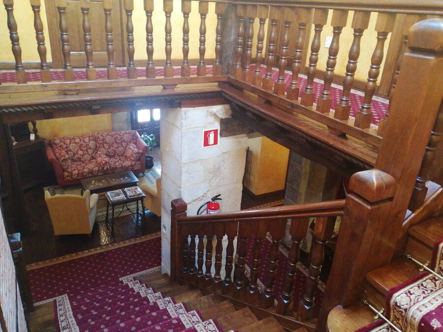 A staircase with a wooden railing, a red fire extinguisher mounted on the wall, a patterned sofa, and a small table with a chair.