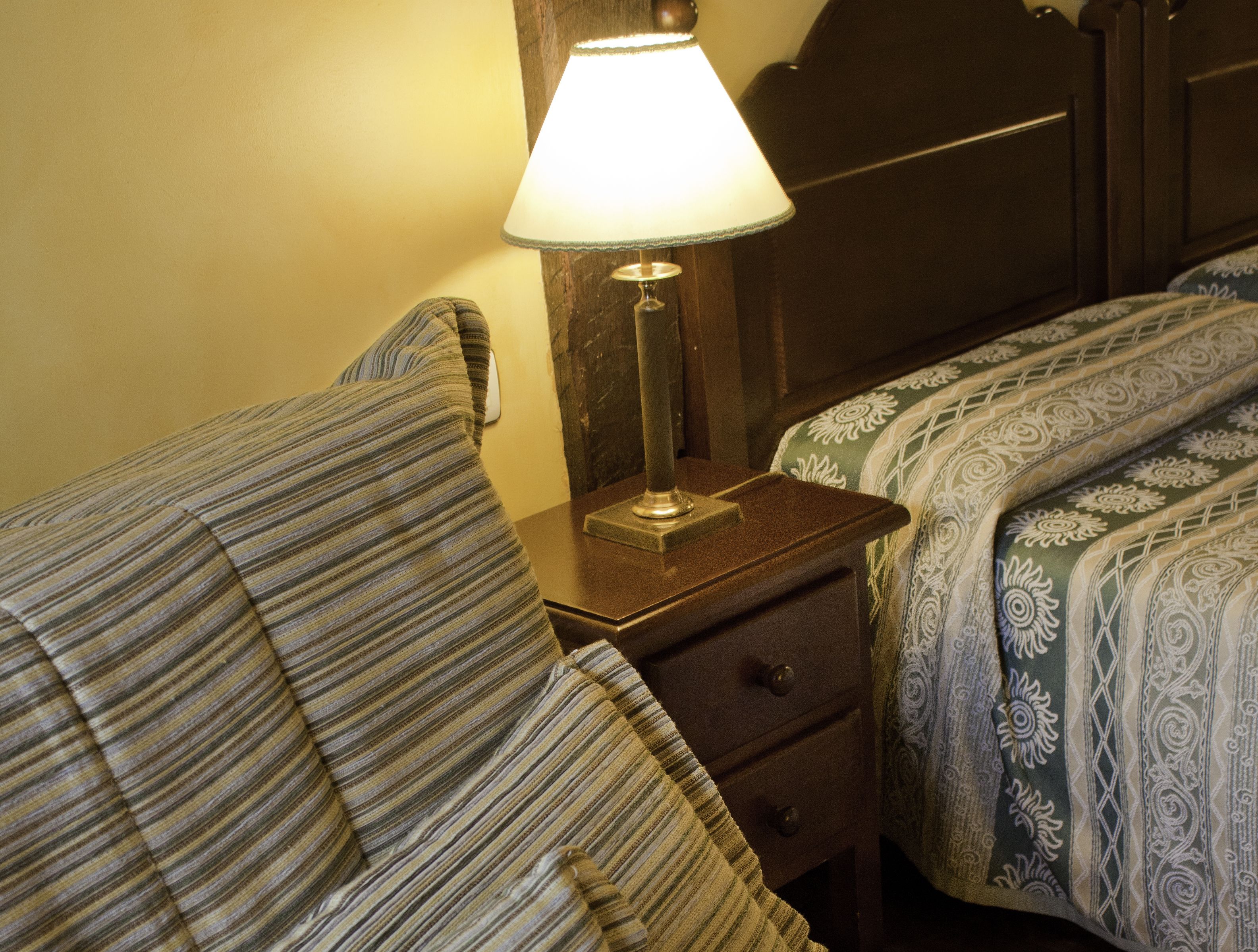 Habitación de hotel con dos camas, cada una con ropa de cama a rayas, una mesita de noche con lámpara y un cabecero de madera.