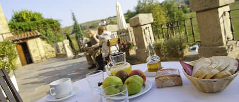 A table set with a white tablecloth, a plate of fruit, a glass pitcher, and a basket of bread.