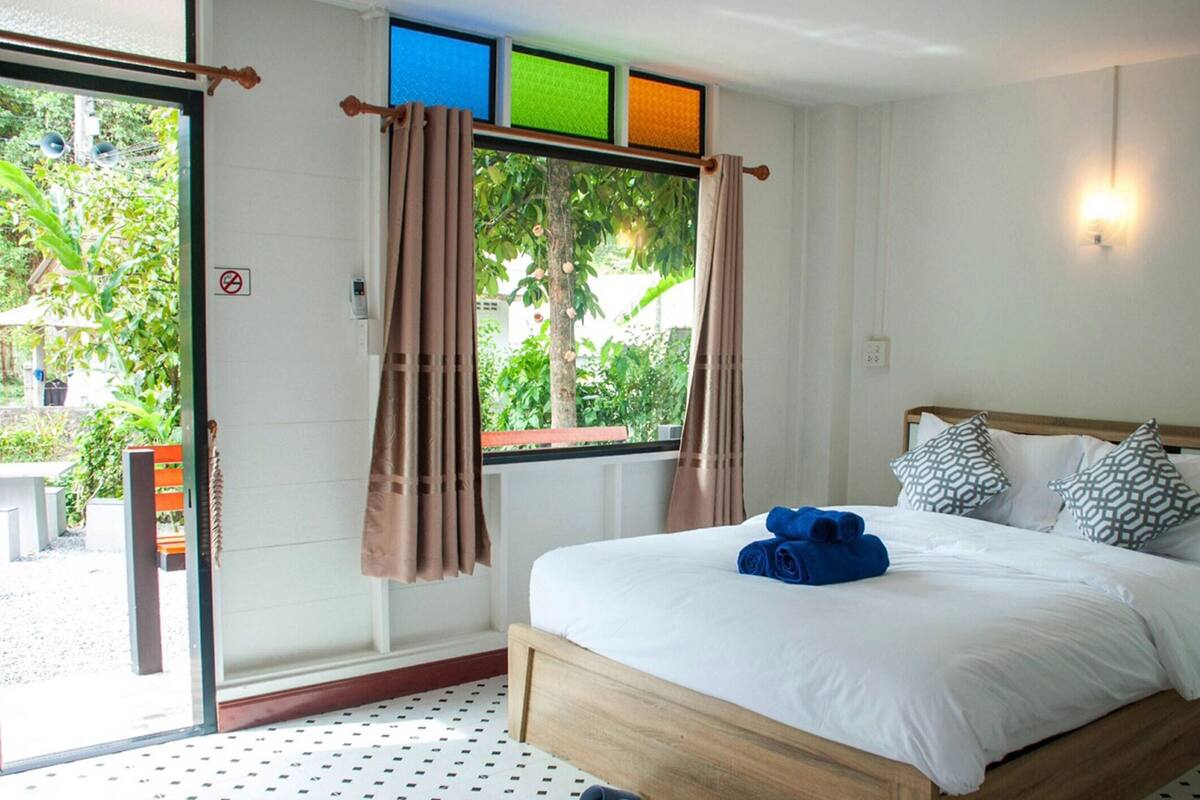 A bedroom with a bed, curtains, a window, and a view of greenery outside.