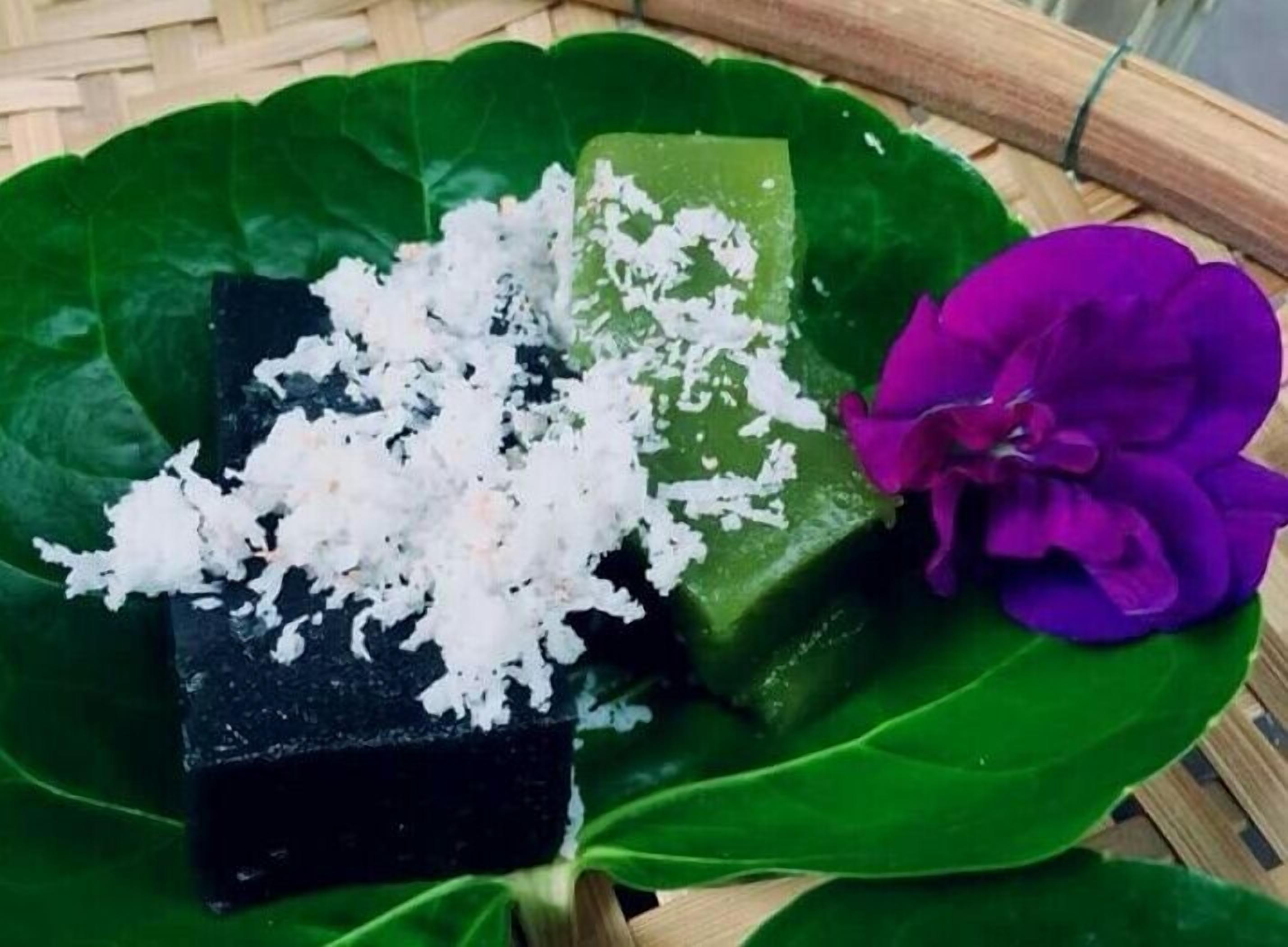 A dessert with a green leaf base, a black cube, and a purple flower.